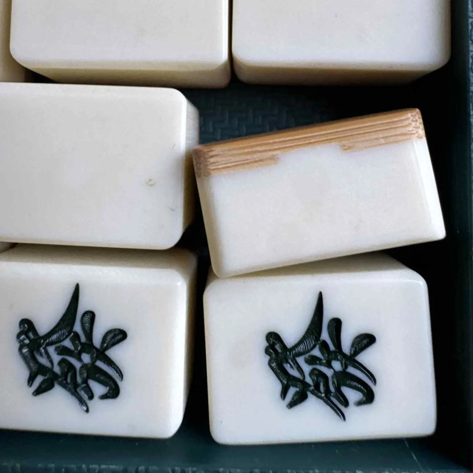 Close-up of white Mahjong tiles with black characters on a dark surface